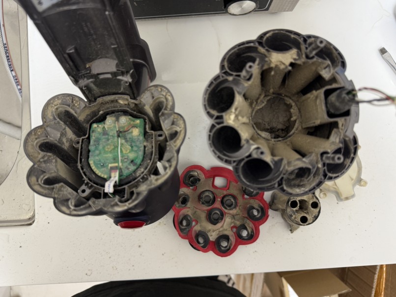 Dyson V12 氣旋組件拆解後,內部錐體與濾網座布滿遇水結塊的灰色硬化塵垢